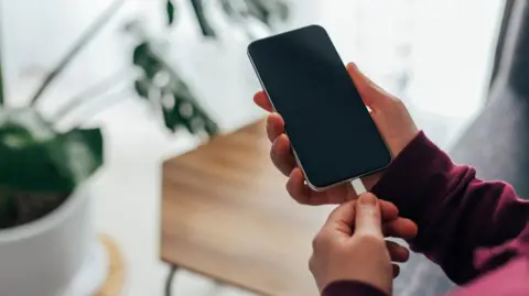 Cambridgeshire Fire and Rescue Service A person holding a black mobile phone in their hand while inserting a white charger.