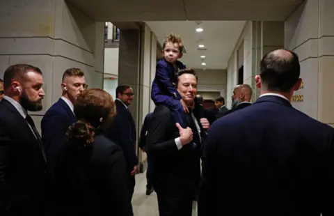 Getty Images Tesla CEO Elon Musk, Co-Chair of the newly announced Department of Government Efficiency (DOGE) carries his son 